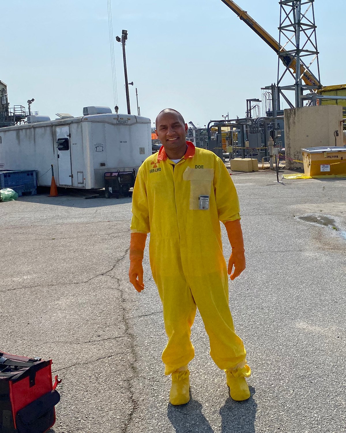 Young man in a bright yellow safety suit and orange gloves standing in an industrial site