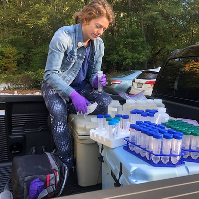 Young woman sitting in the back of a pickup truck wearing gloves and handling vials